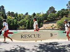 Three lifeguards walking holding a rescue board 