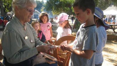 Docent at Ardenwood Farm demonstrating spinning yarn to a group of children
