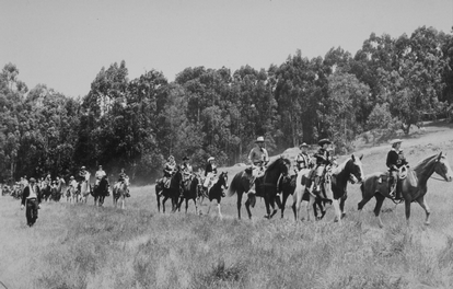 a group of people riding gorses througha field with trees in the background