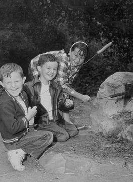 three children with hot dogs on sticks, smiling b&w