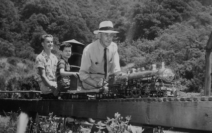 one adult and two children riding in a small train b&w